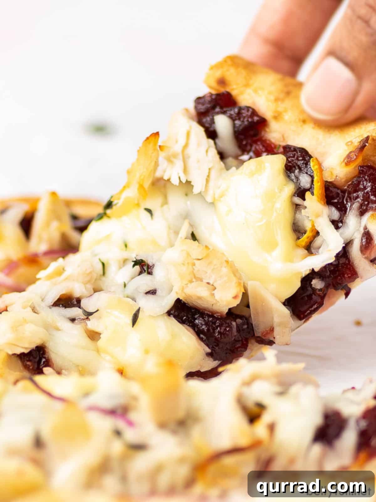 A hand pulling apart a piece of naan pizza with brie cheese stretching, showing the gooey texture