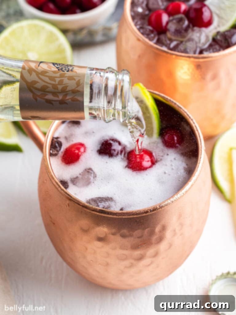 Ginger beer being poured into a copper mug filled with ice and other ingredients.