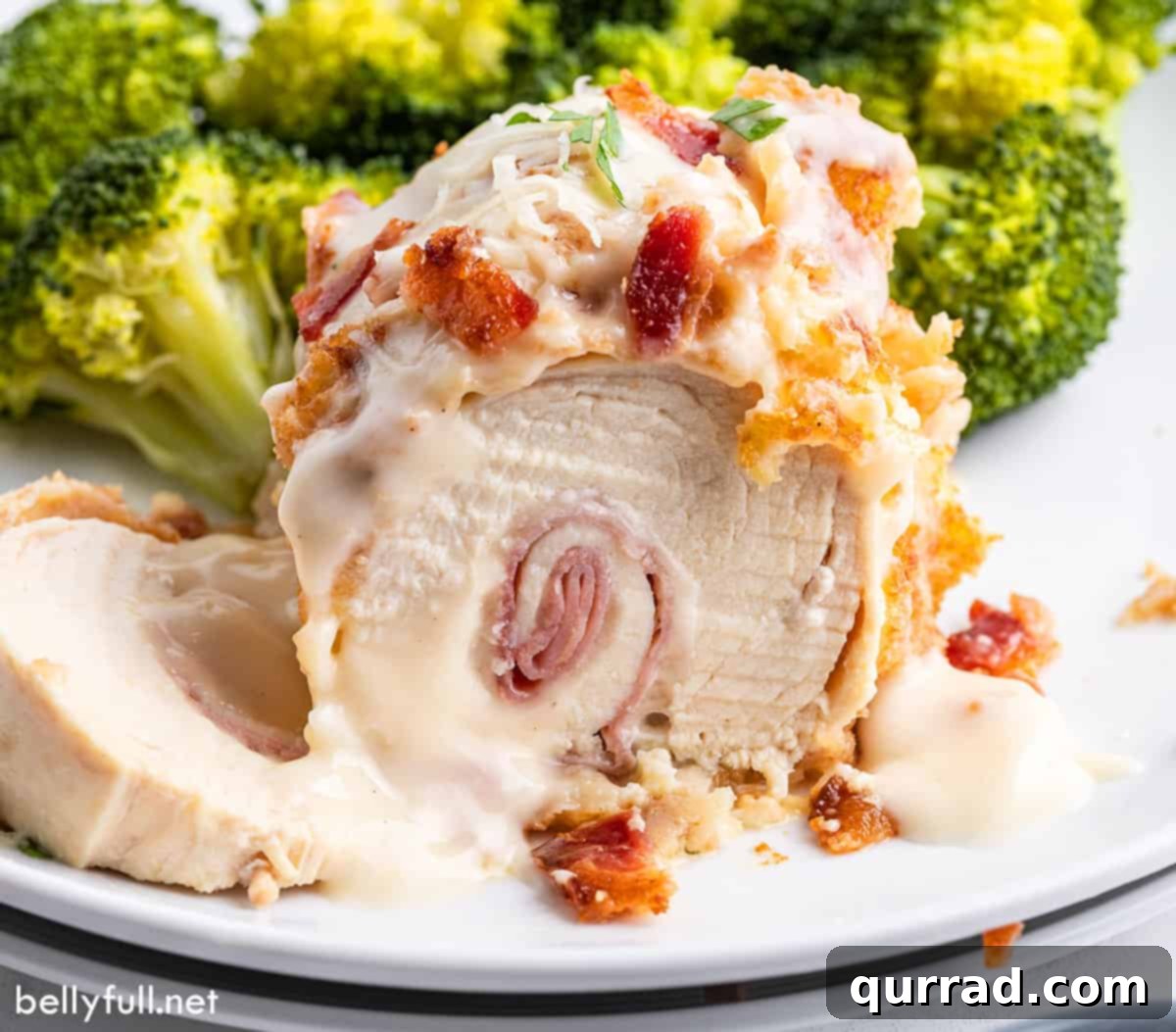 Golden Chicken Ham and Swiss 12 Chicken cordon bleu on a white plate with roasted broccoli, drizzled with sauce.
