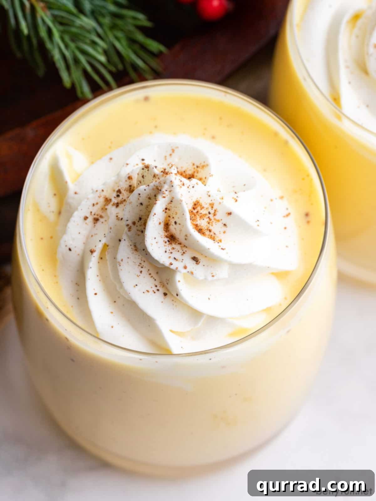 Winter Warmer Eggnog 4 A close-up of a glass of homemade eggnog, richly topped with creamy whipped cream and a sprinkle of fresh nutmeg, ready to be savored.
