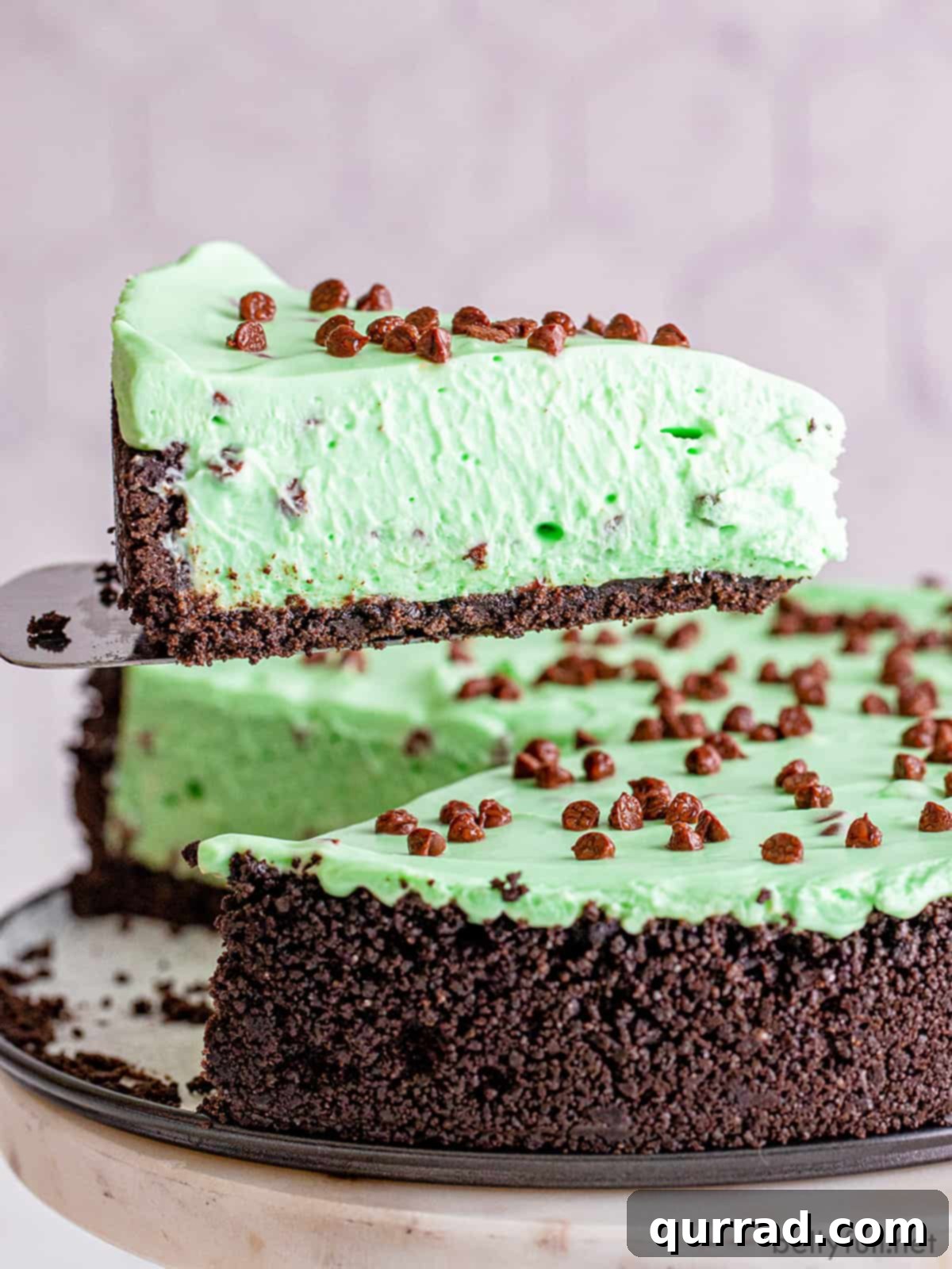 Effortless Mint Chocolate Chip Cheesecake 5 A slice of Mint Chocolate Chip No Bake Cheesecake being served on a white plate, highlighting its smooth green layer.