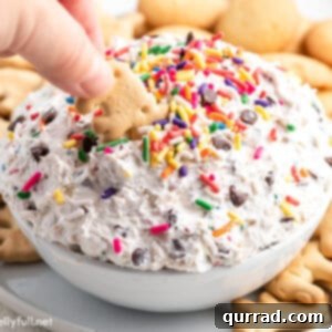 A hand dipping an animal cracker into Funfetti Dip, ready to be enjoyed.
