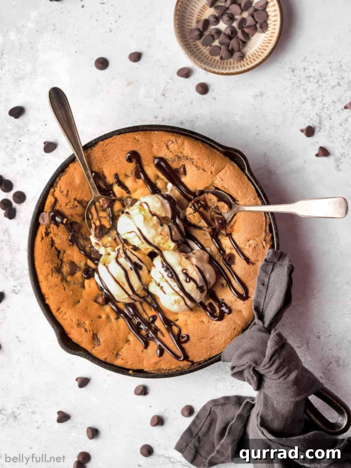 Overhead view of a chocolate chip skillet cookie, generously topped with melting ice cream and flowing chocolate syrup