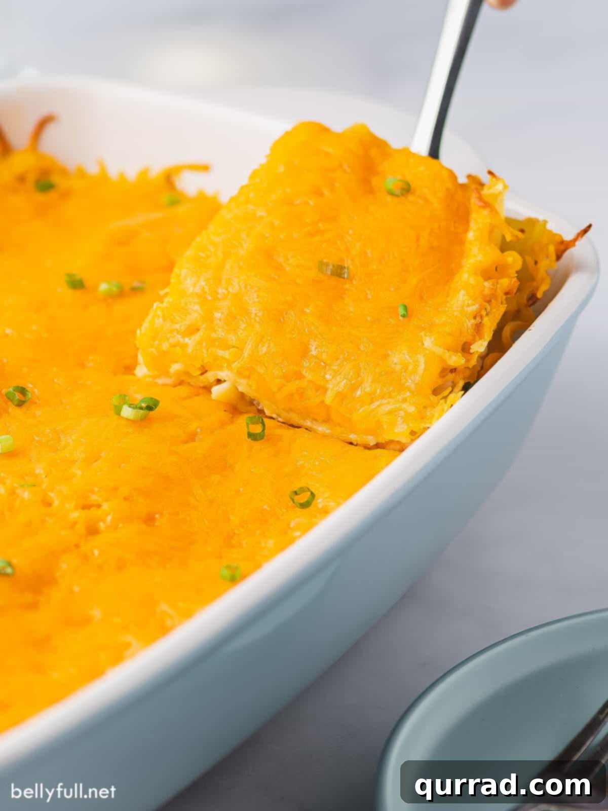 A spatula scooping a slice of golden-brown pierogi lasagna from a glass baking dish, revealing its creamy, cheesy layers.
