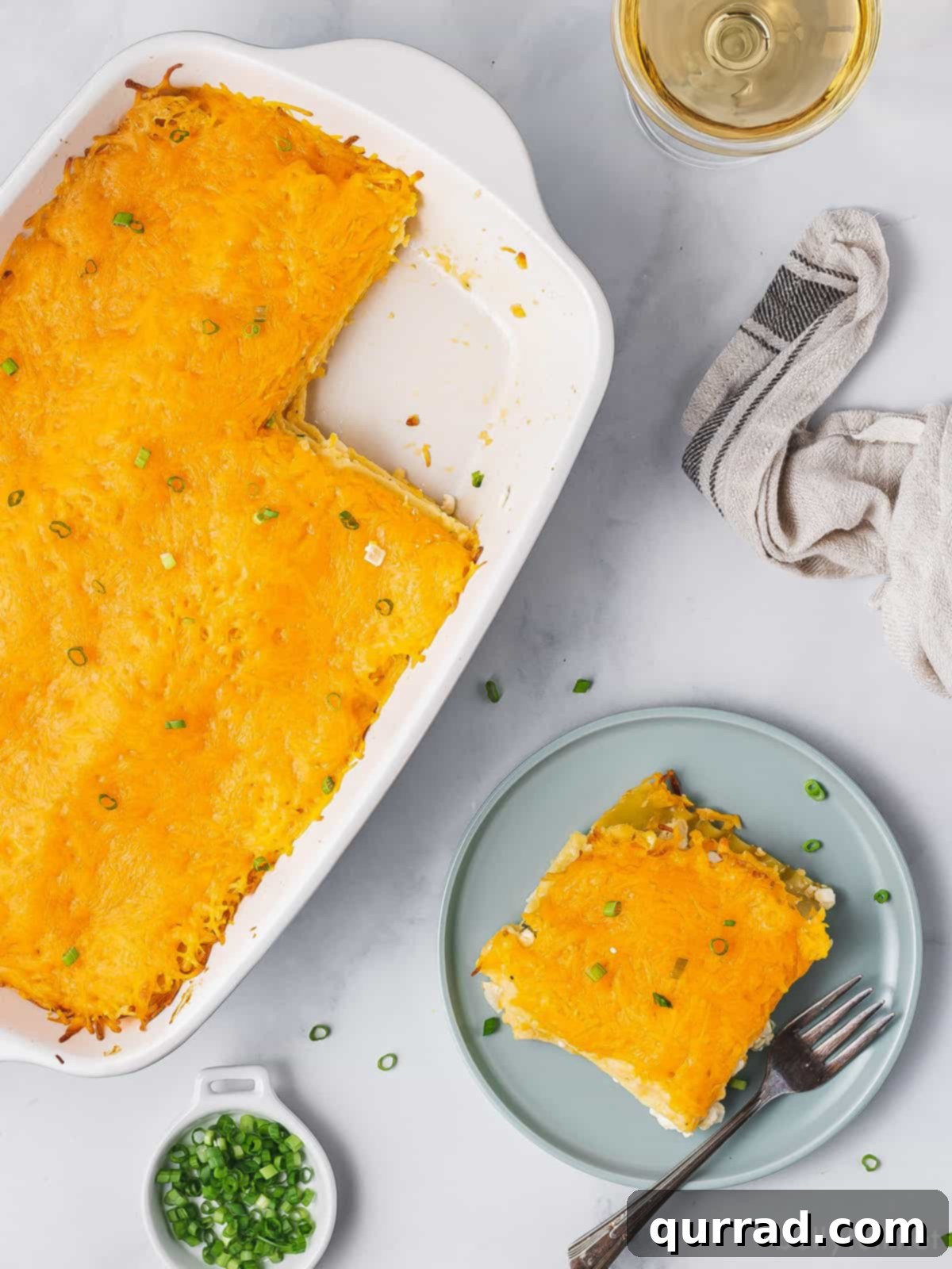 Overhead view of a pierogi lasagna in a baking dish with one perfectly sliced portion on a blue plate, ready to be served.