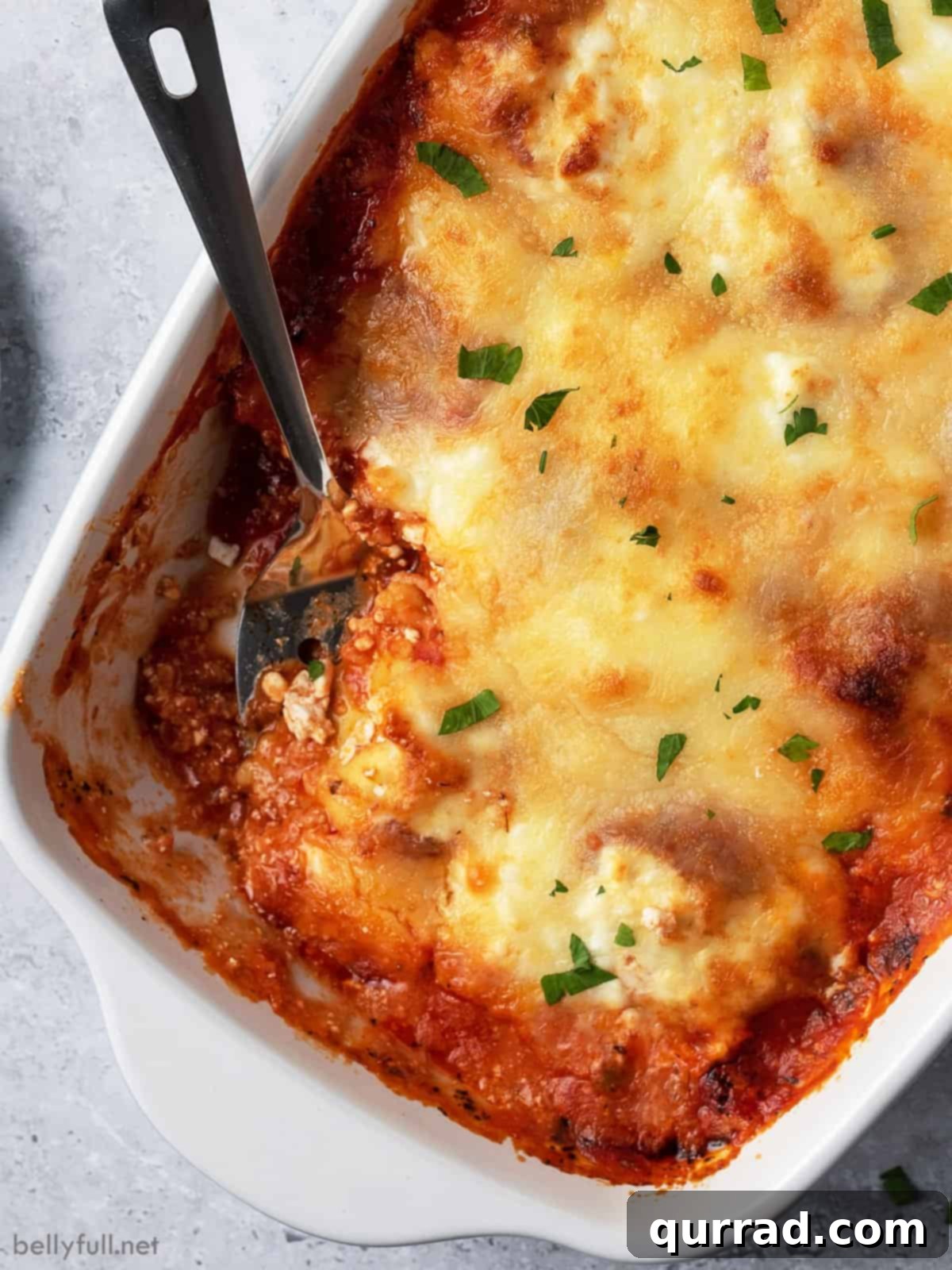 Cheesy Ravioli Dream 4 A spoon digging into a warm baked ravioli casserole, showing layers of pasta, sauce, and melted cheese.