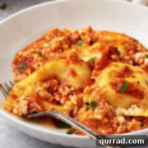 Cheesy Ravioli Dream 6 A white bowl of ravioli casserole with a fork on the dish, garnished with fresh parsley.