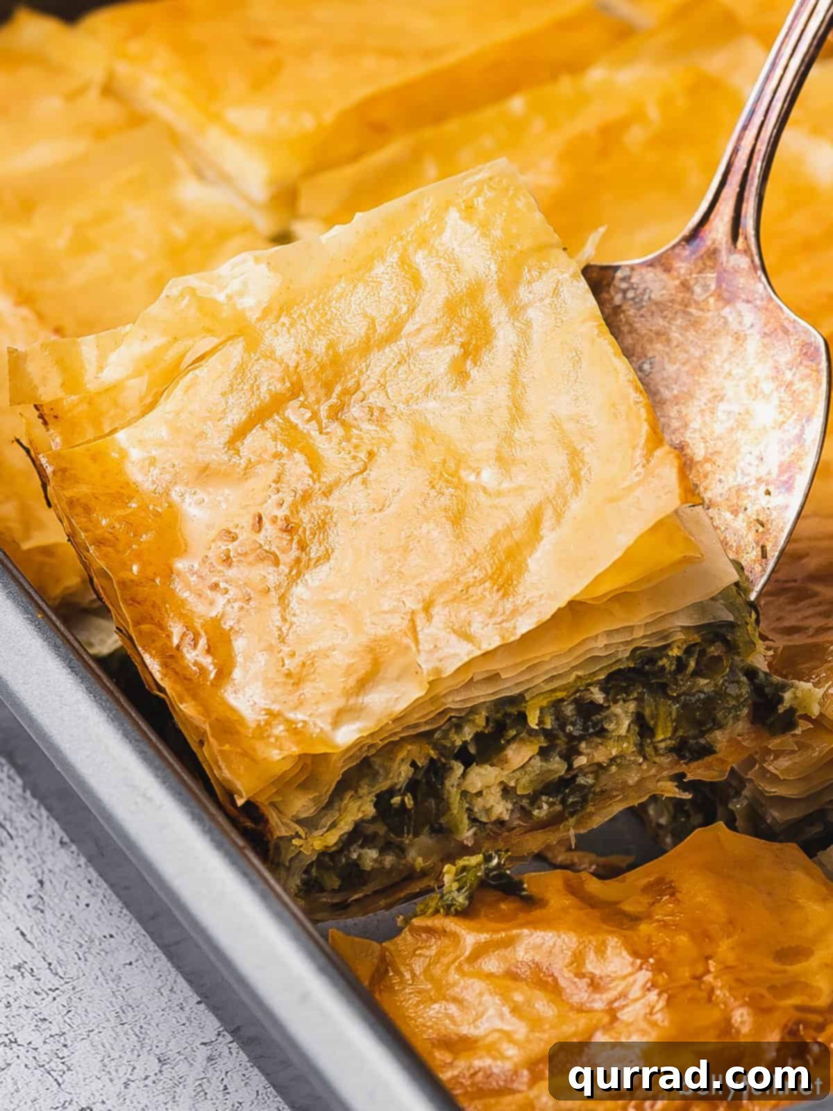 A spatula carefully scooping out a perfectly golden square of Greek spinach pie, ready to be served.