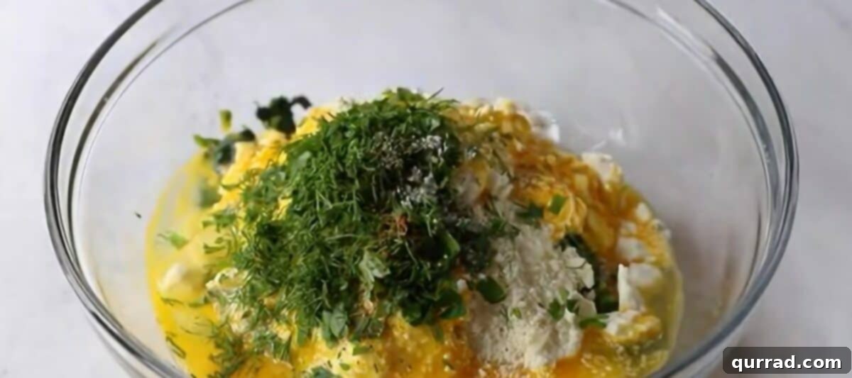 A glass bowl filled with all the vibrant ingredients for the spanakopita filling, including spinach, cheeses, and herbs.