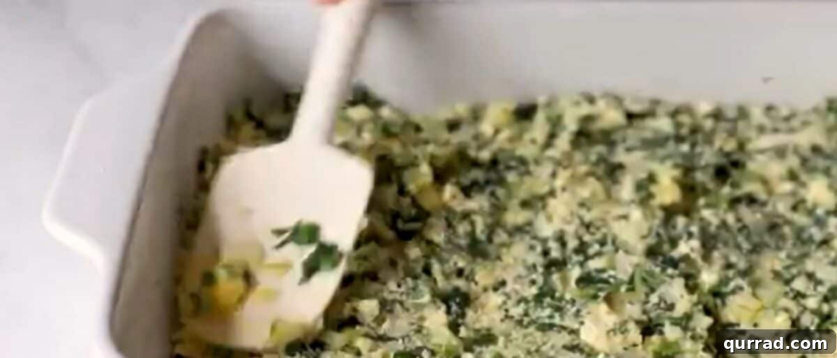 The savory spinach and cheese filling being spread evenly over the phyllo dough crust in a baking dish.