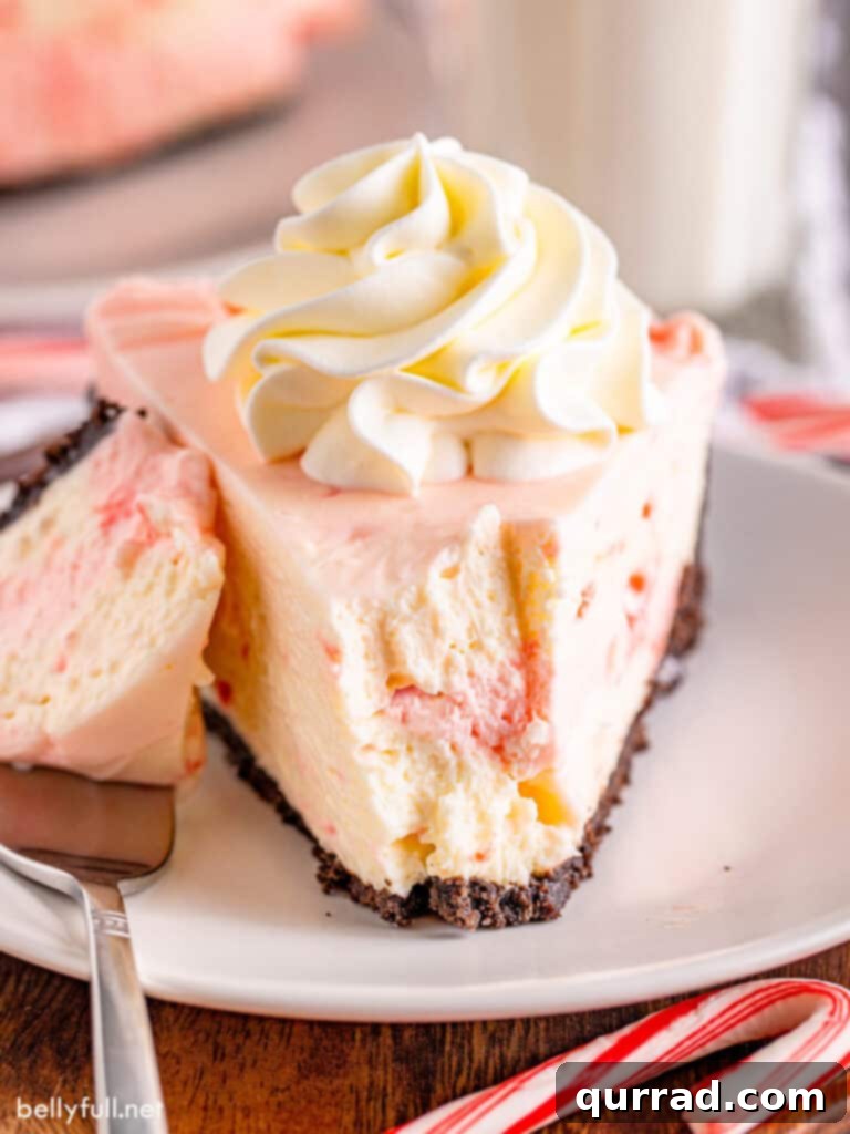 Front angle view of a no-bake peppermint cheesecake with a slice taken, showcasing its creamy pink and white layers and cookie crust.