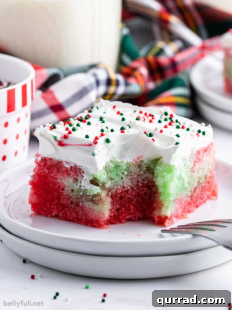 Jiggly Holiday Poke Cake 5 A square piece of Christmas Jello Poke Cake on a plate with a bite taken, revealing the moist, colorful interior.