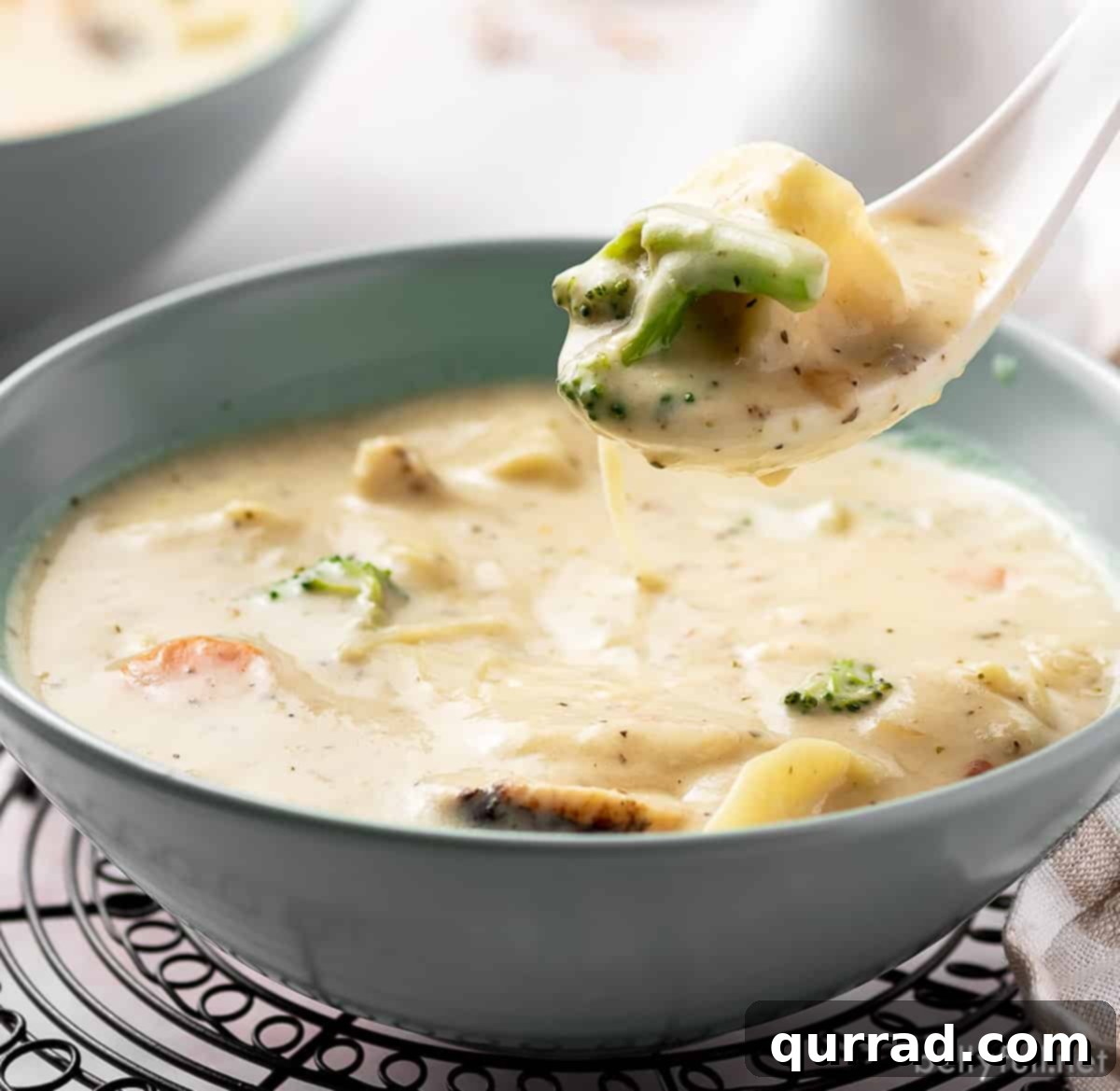 Creamy Parmesan Chicken Tortellini Soup 5 A spoonful of chicken alfredo tortellini soup held over a bowl, highlighting the tender chicken and tortellini.