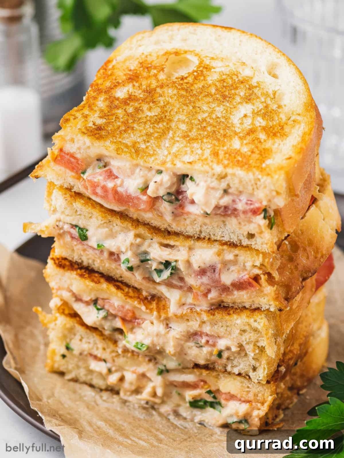 Gourmet Tuna Grilled Cheese 3 Four halves of a grilled tuna melt sandwich, stacked neatly, showcasing the layers of tuna, tomato, and melted cheese between slices of rustic bread.