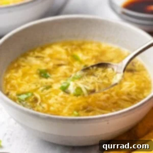 A bowl of egg drop soup with a spoon held over it, ready to be enjoyed.