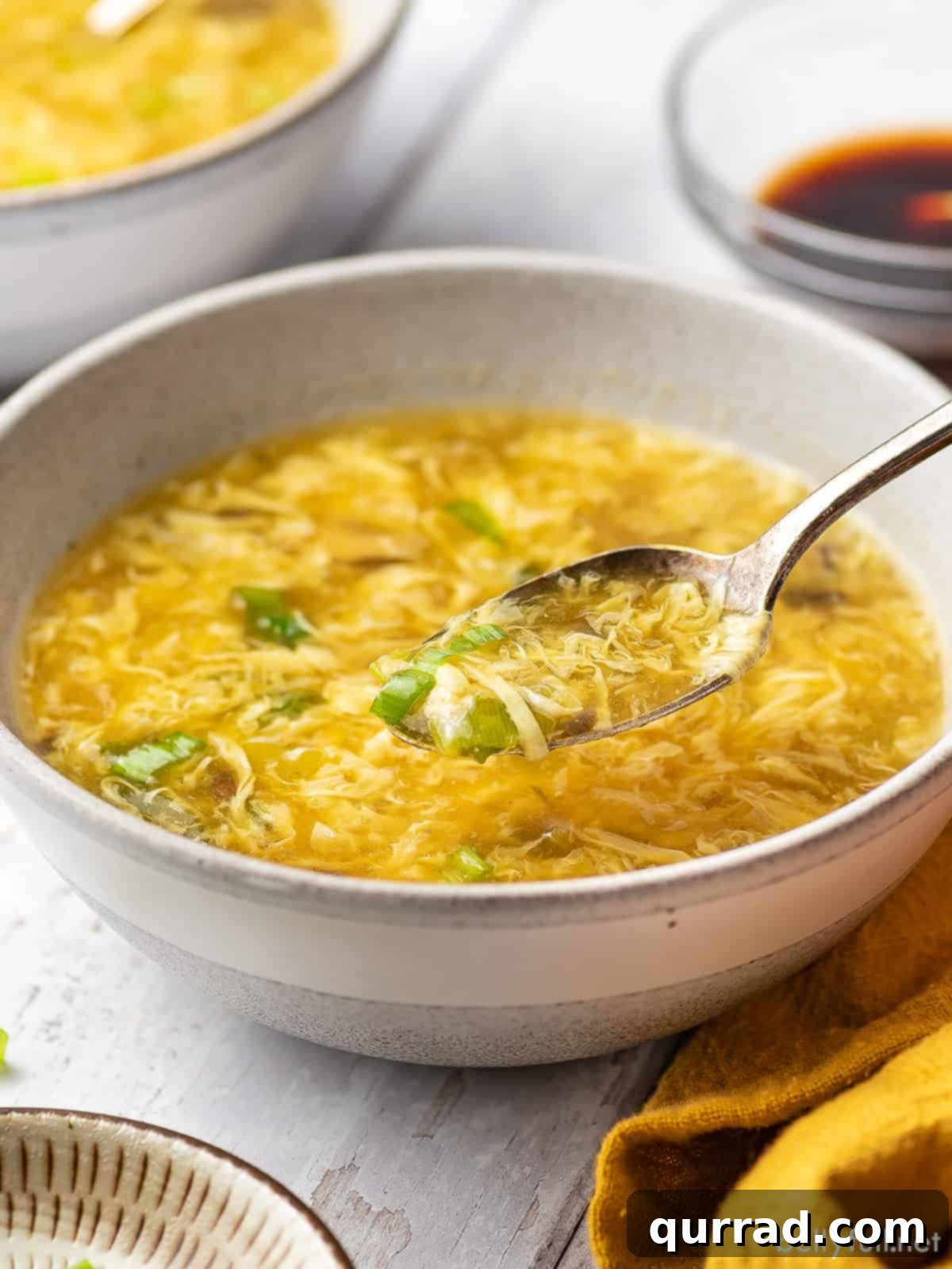 Classic Egg Drop Soup 6 A close-up view of a bowl of homemade egg drop soup with a spoon, highlighting the delicate egg ribbons.