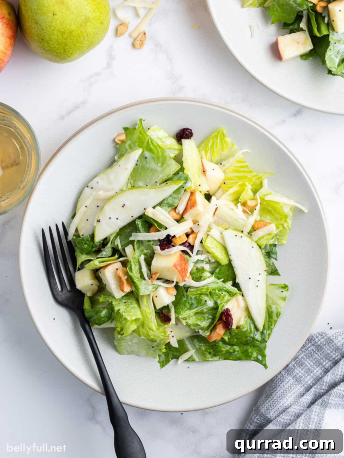 A single serving of pear salad on a white plate, garnished with extra cranberries, with a serving spoon nearby.
