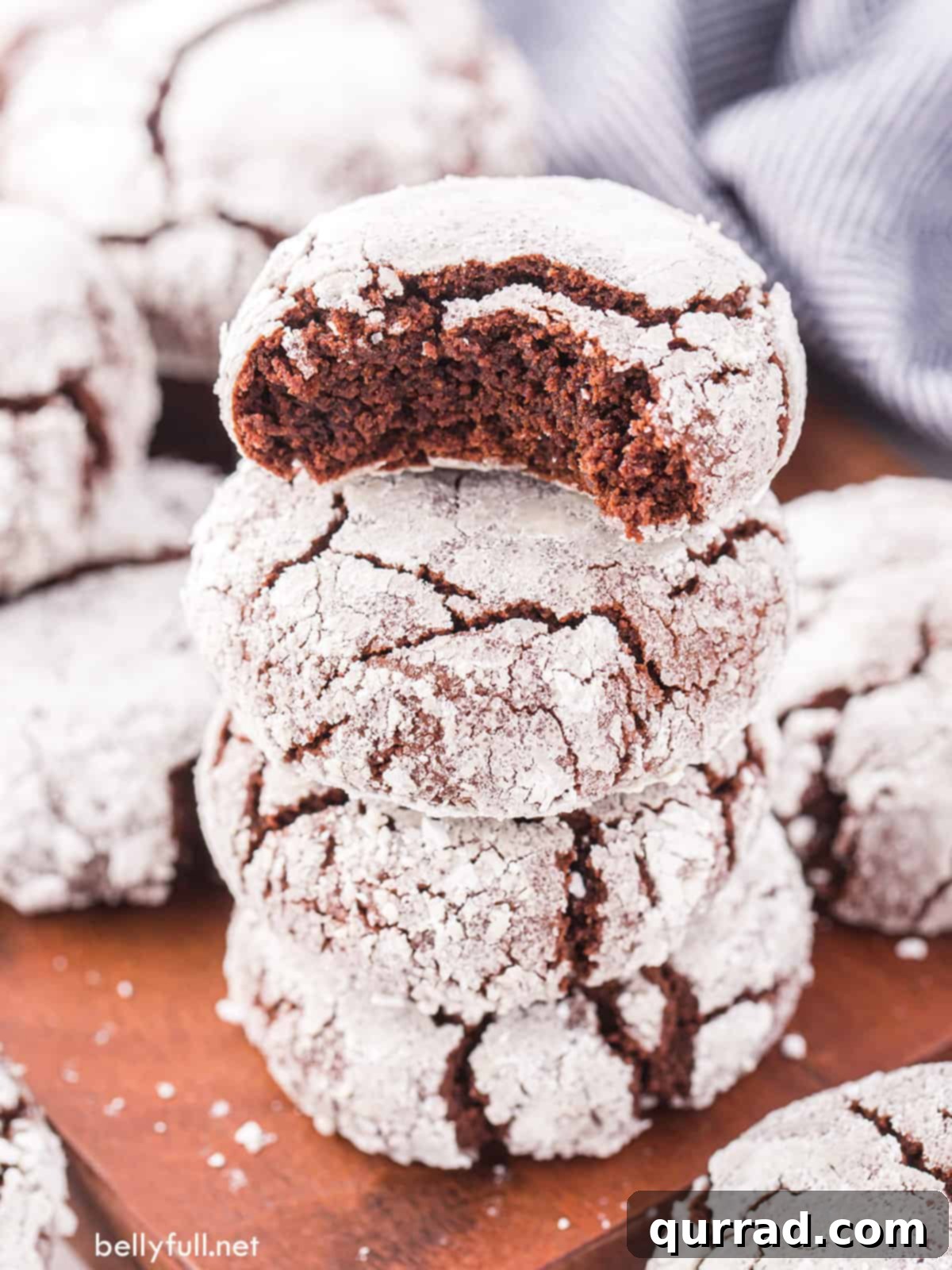 Fudgy Chocolate Crinkles 6 Four chocolate crinkle cookies on a wooden board, one with a bite taken out, showing its rich, moist interior.