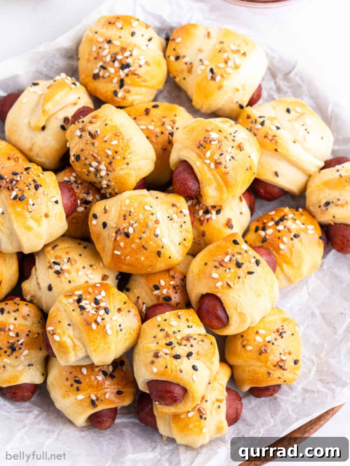 Cozy Canine Bites 2 Overhead view of a pile of mini pigs in a blanket, garnished with fresh herbs and a scattering of everything bagel seasoning.