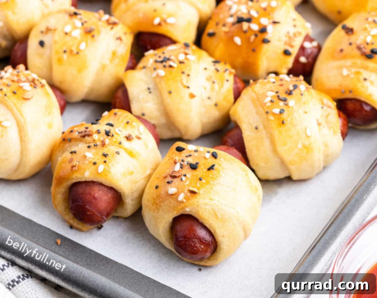 Cozy Canine Bites 3 Mini pigs in a blanket cooling on a parchment-lined baking sheet, showing their perfectly golden and crispy crusts.