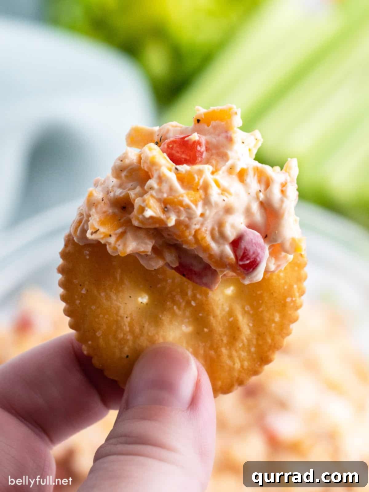 Fingers holding a buttery Ritz cracker that has been generously dipped into a bowl of creamy pimento cheese, ready to be enjoyed.