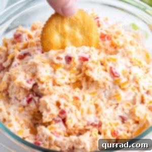 A close-up of a hand dipping a cracker into the rich and textured pimento cheese dip.