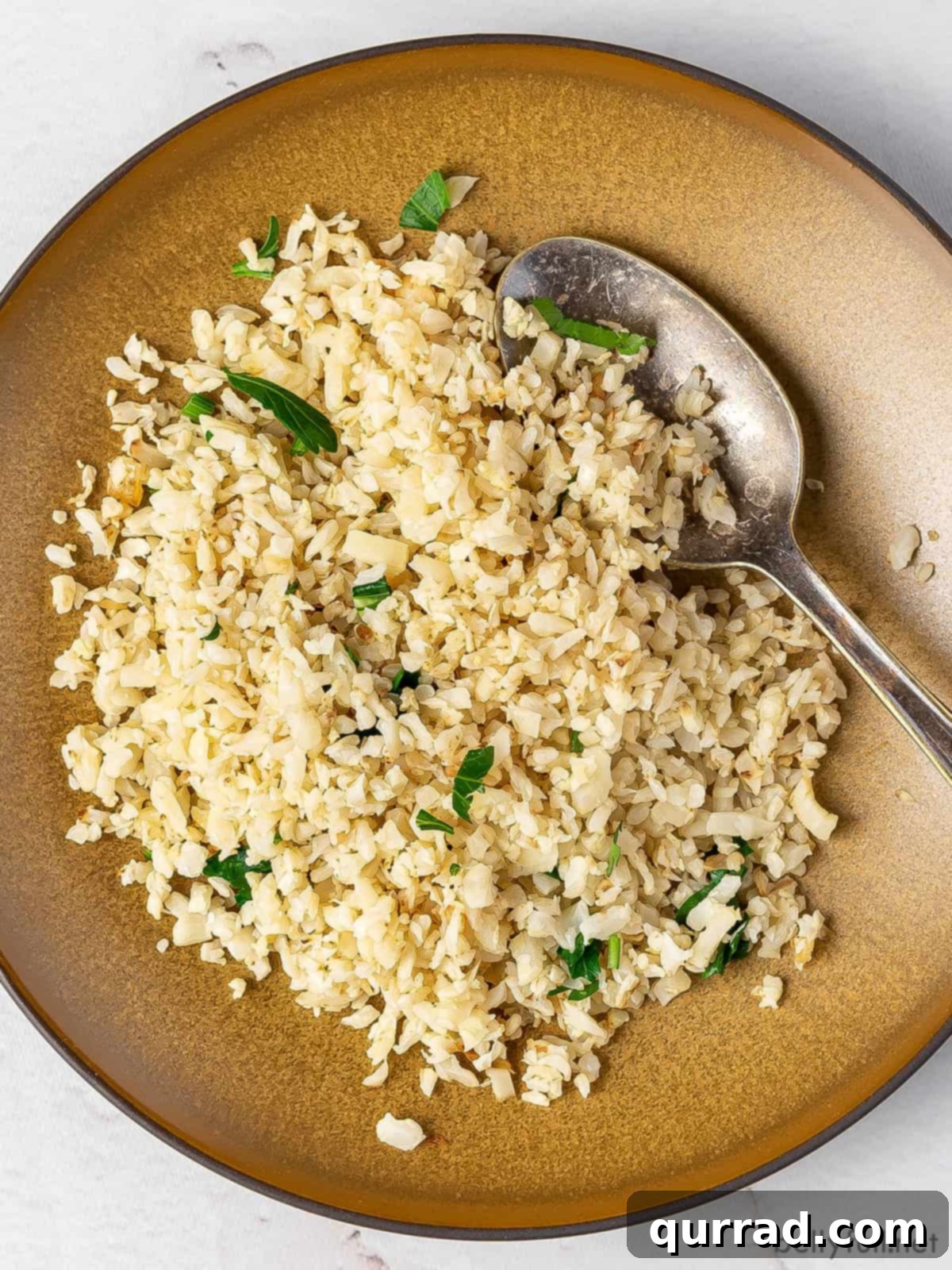 Wholesome Cauliflower Grains 2 Overhead view of perfectly cooked cauliflower rice on a brown plate with a spoon, ready to serve.