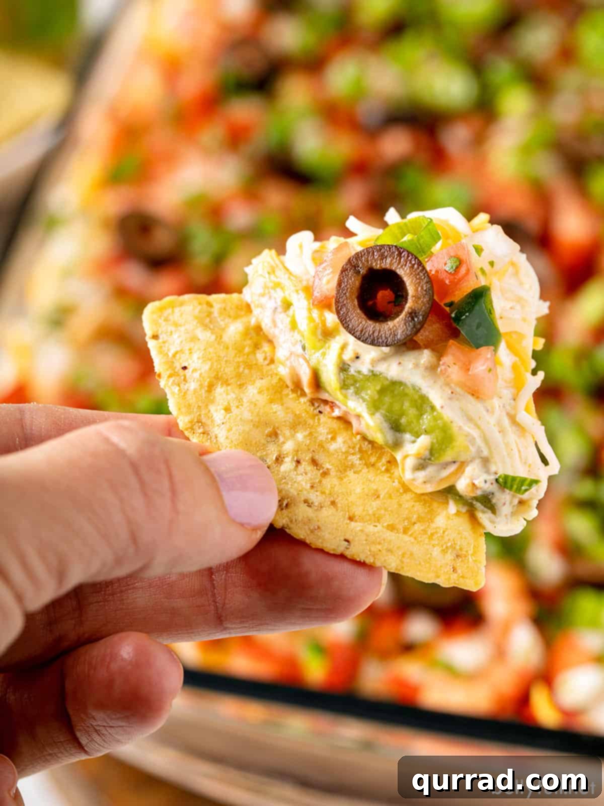 Ultimate Seven-Layer Dip 11 A hand holding a tortilla chip perfectly scooping a portion of 7 layer dip.