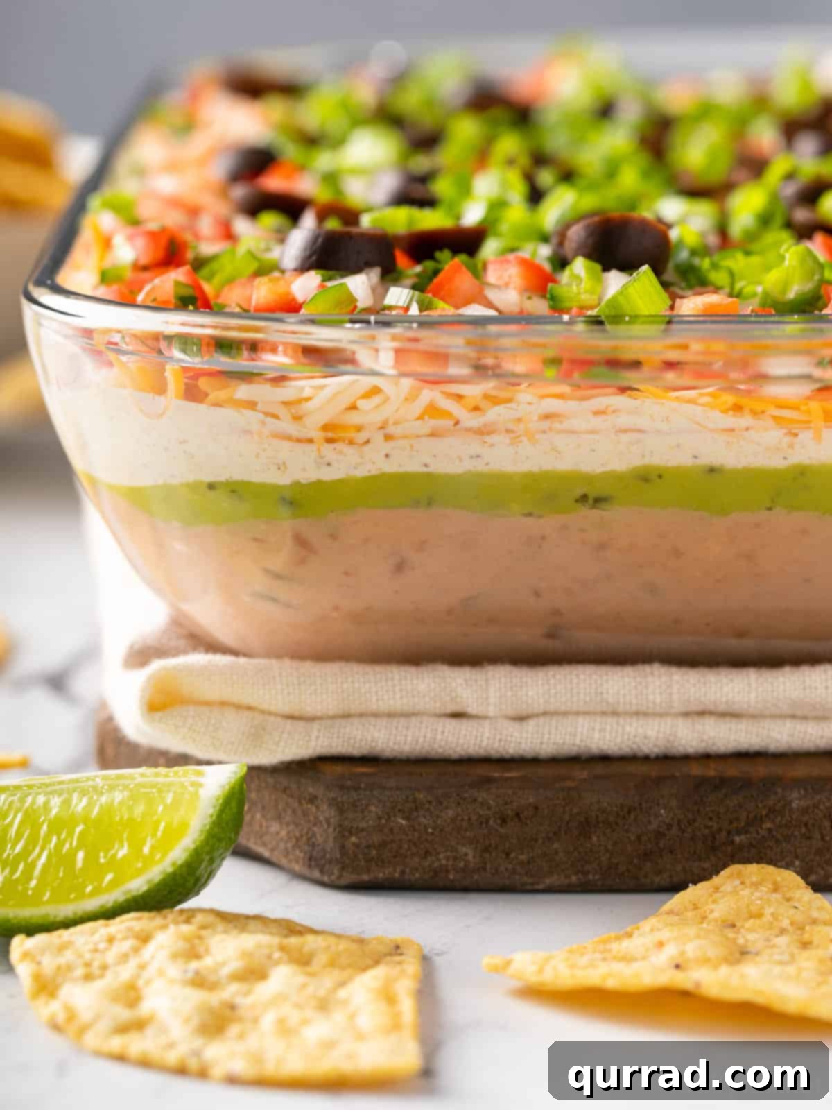 Ultimate Seven-Layer Dip 13 Angled view of a casserole dish showing the layers of 7 layer taco dip, ready for a party.
