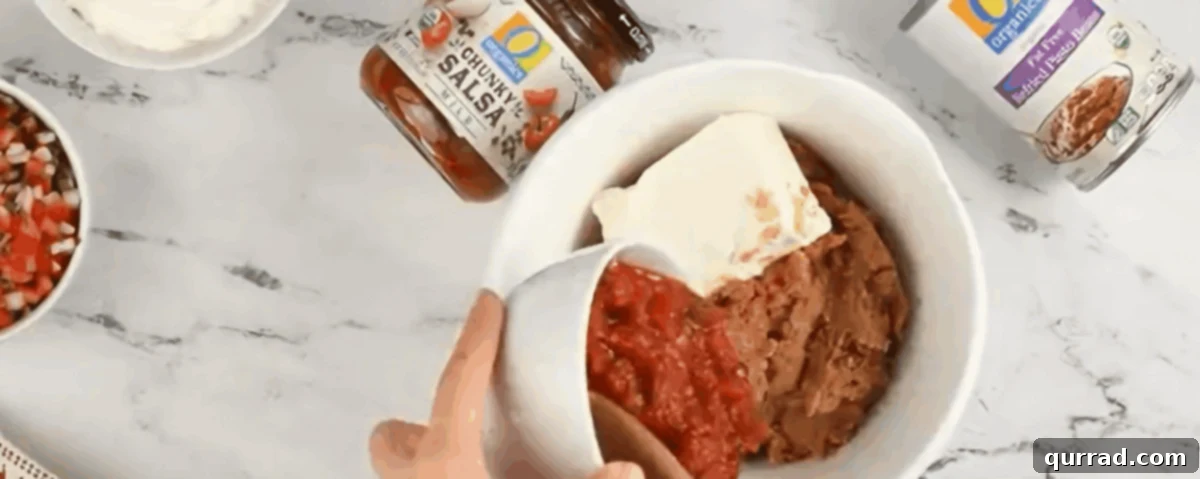Ultimate Seven-Layer Dip 6 Preparing the bean layer with refried beans, cream cheese, and salsa in a mixing bowl.