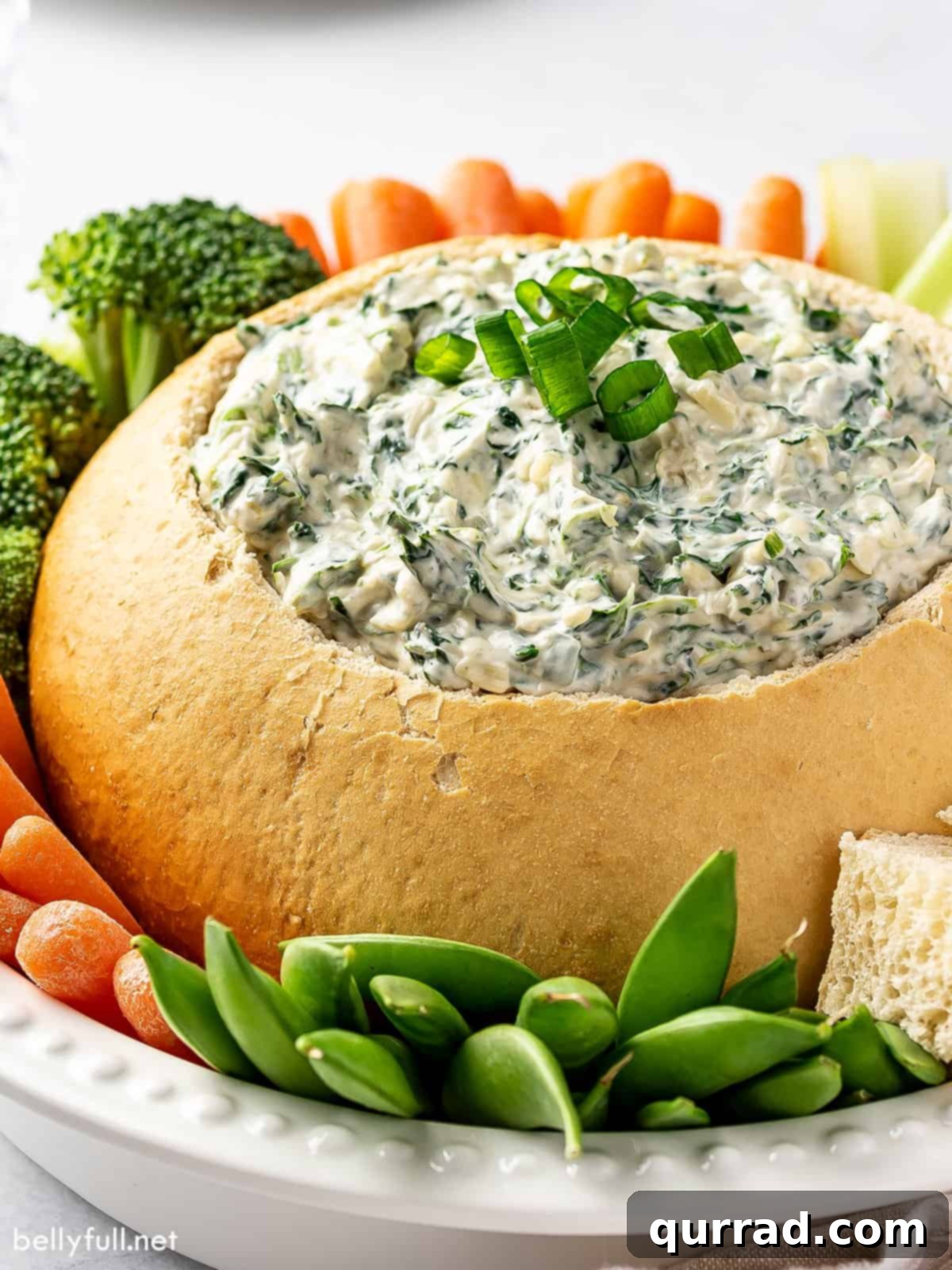 Creamy Spinach Dream 4 Spinach dip in a beautifully carved sourdough bread bowl, surrounded by a vibrant array of fresh vegetables like carrot sticks, cucumber slices, bell pepper strips, and broccoli florets, along with cubed sourdough bread, ready for dipping at a party.