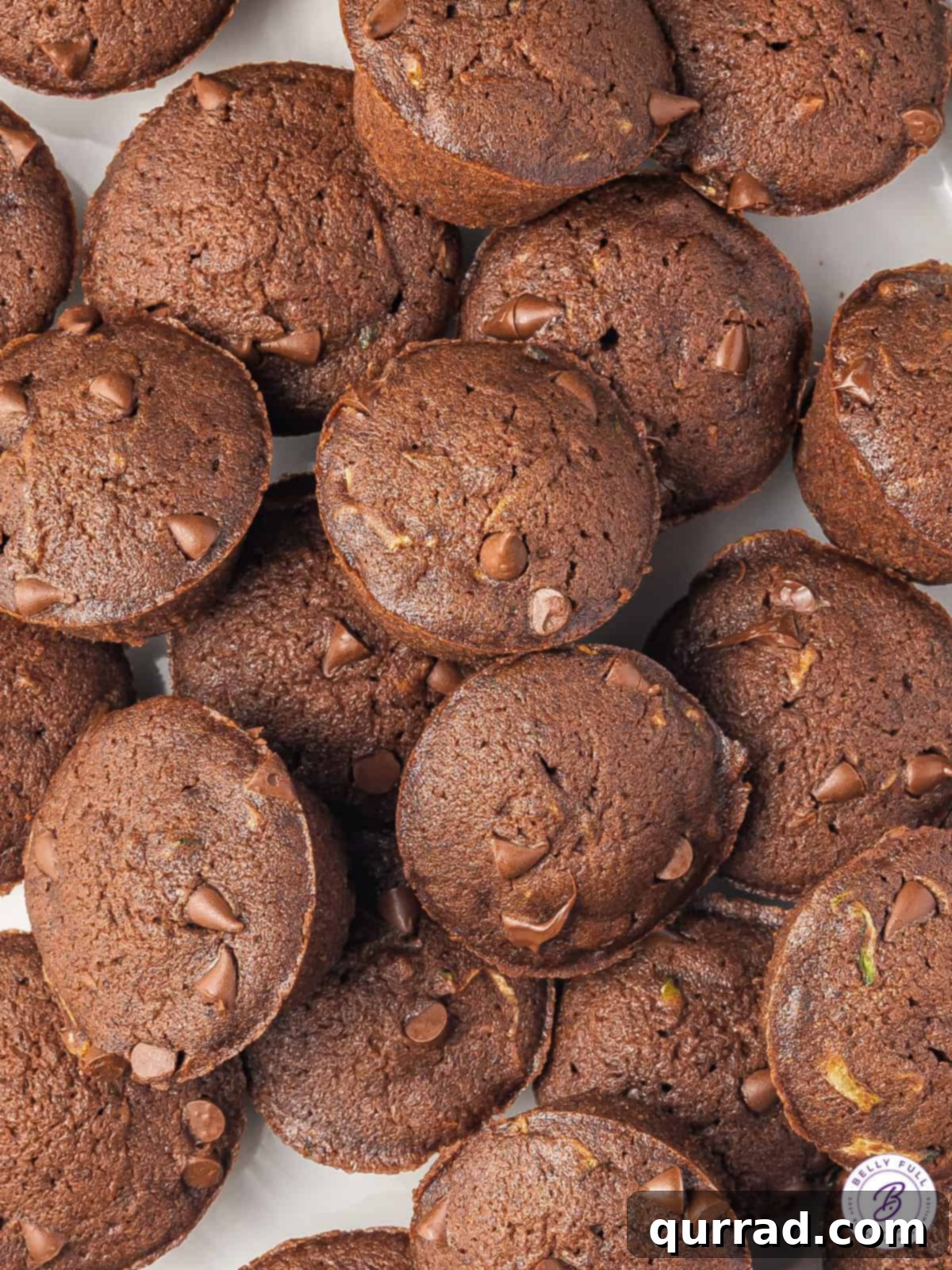 A close-up of several mini chocolate zucchini cakes, showing the intricate speckles of zucchini and the rich, dark chocolate color.