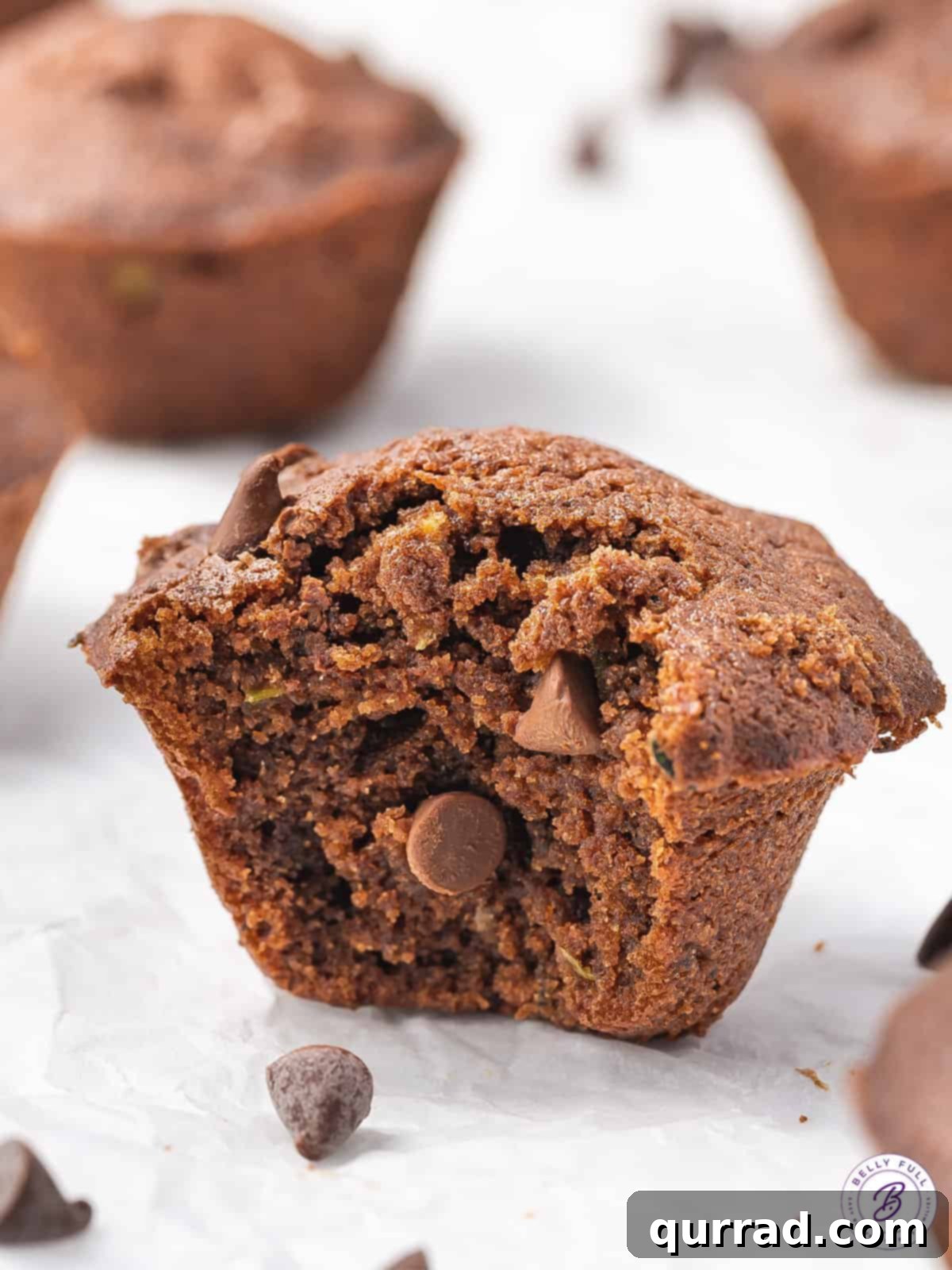 A mini chocolate zucchini cake with a bite taken out, revealing its moist interior and chocolate chips, against a blurred background.