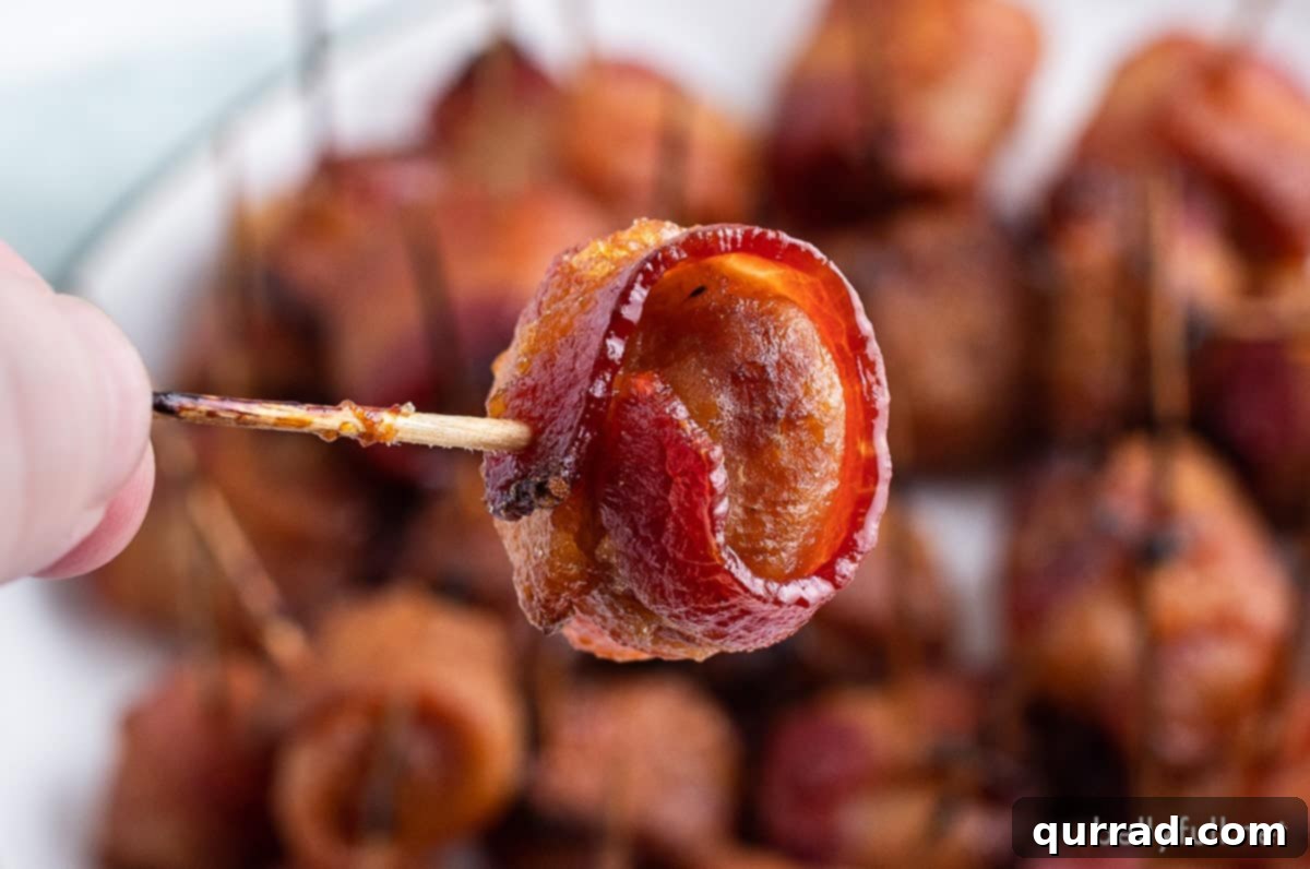 A toothpick holding a bacon wrapped water chestnut, showing the crispy bacon and glistening marinade