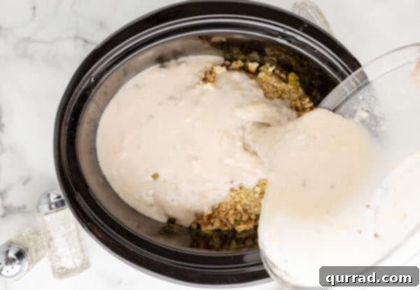 Creamy sauce being poured over chicken and stuffing layers in crockpot