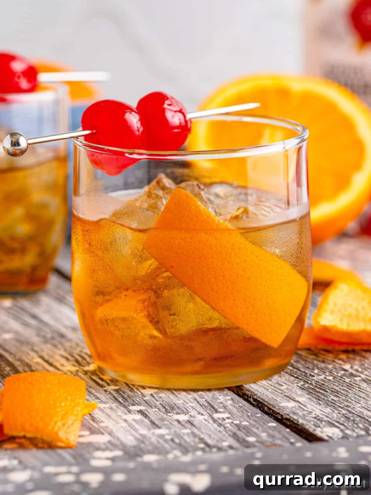 Timeless Elegance 4 Side view of an old fashioned cocktail with a large ice cube, garnished with a vibrant orange peel and two maraschino cherries.