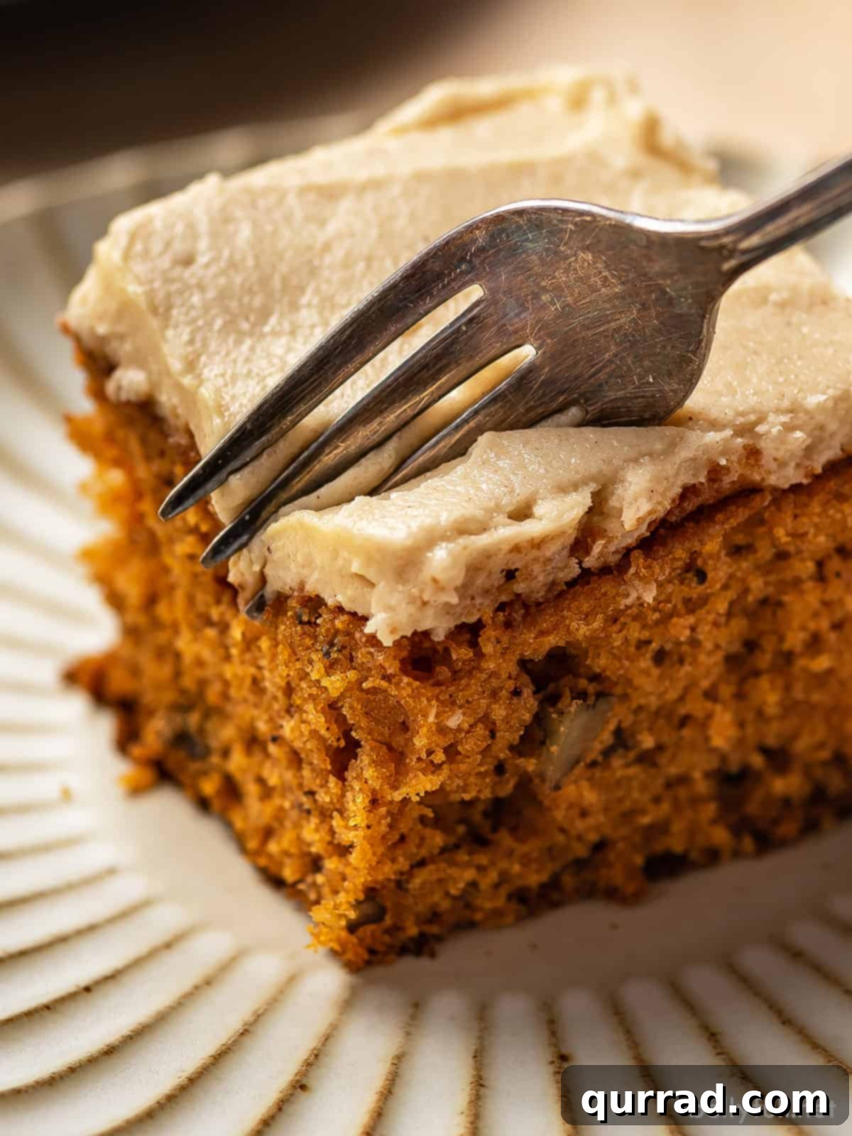 Velvet Tomato Spice Cake 2 A fork gently slices into a piece of frosted Tomato Soup Cake, revealing its moist and tender interior. The rich brown sugar frosting glistens enticingly, promising a delightful bite.