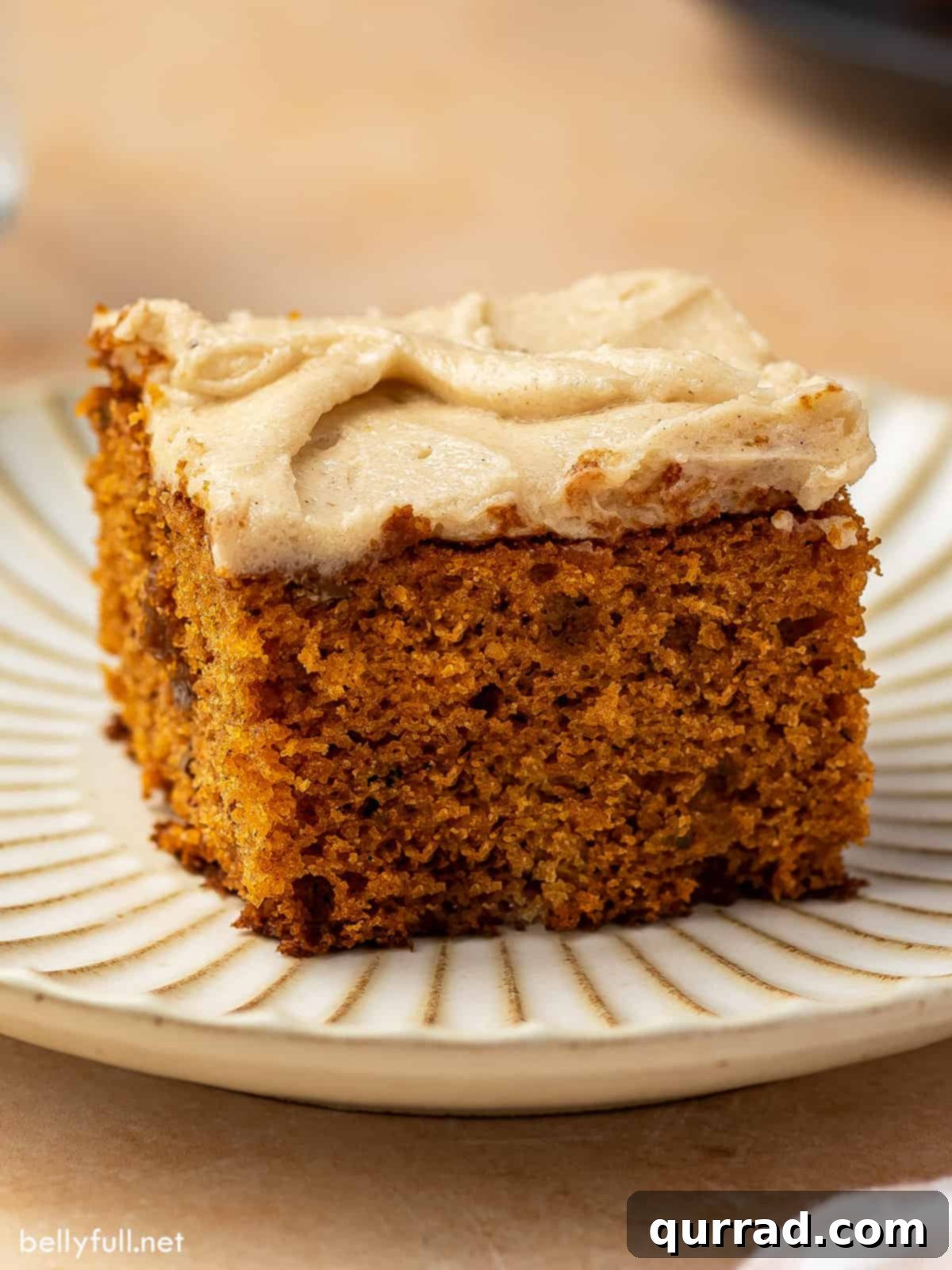 Velvet Tomato Spice Cake 5 A square piece of frosted spice cake elegantly presented on a white plate. The soft brown sugar frosting and moist texture are evident, promising a delicious dessert experience.