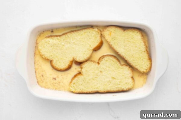 Decadent Challah French Toast 7 Three slices of challah bread soaking in the egg custard within a casserole dish.