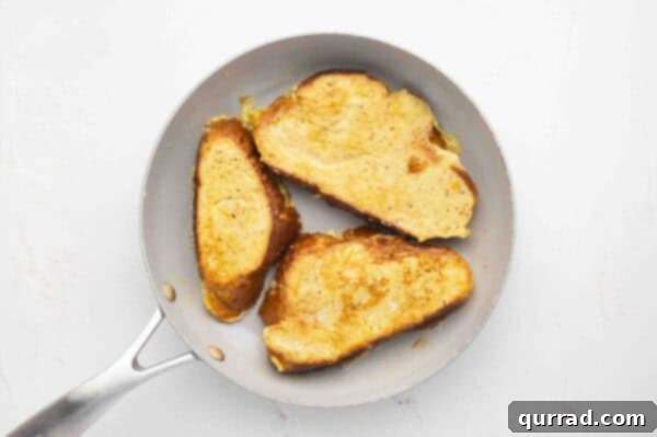 Decadent Challah French Toast 8 Three slices of challah French Toast cooking in a frying pan until golden brown.