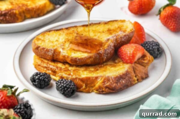 Decadent Challah French Toast 9 Two pieces of French toast with maple syrup being drizzled over them.