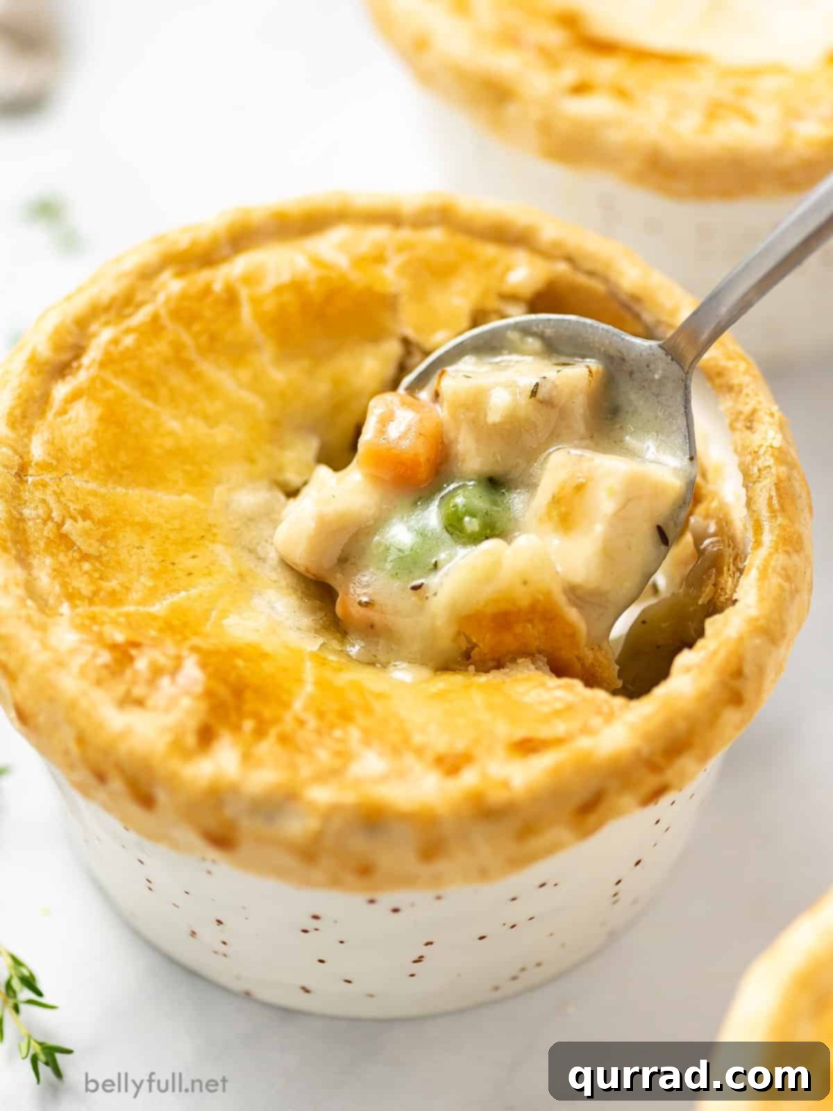 A spoon scooping into a mini chicken pot pie, showing the creamy filling and flaky crust