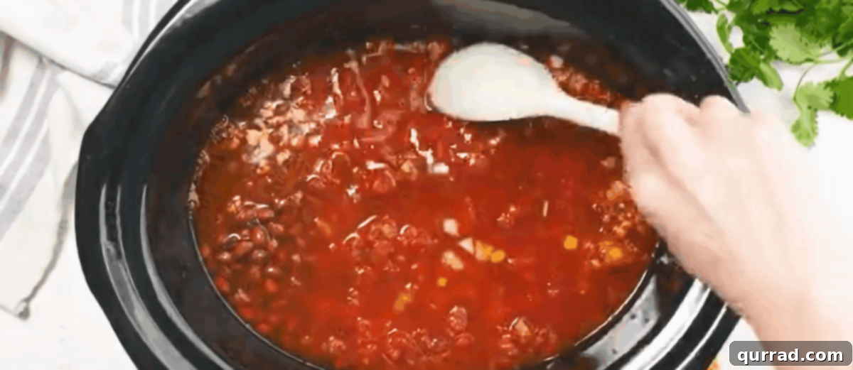 Combining the ingredients to make chicken taco soup in a black crockpot.