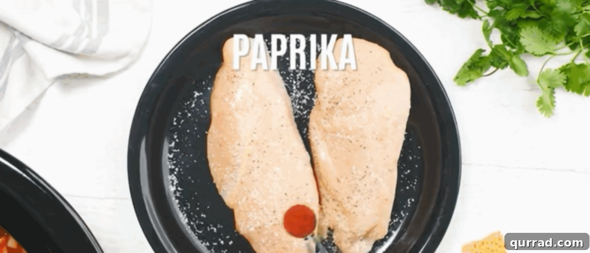 Seasoning chicken breasts on a black plate. 
