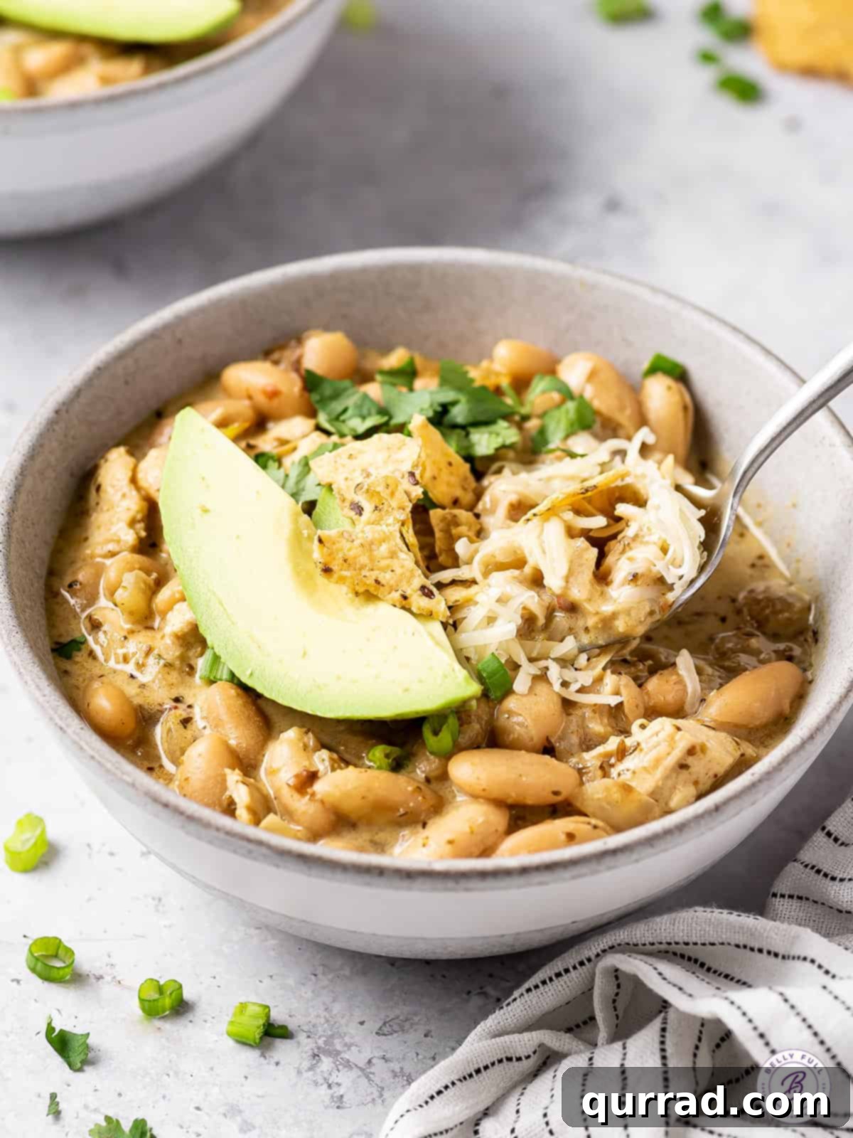 Smoky White Chicken Chili 5 Angled view of a bowl of white chicken chili with a spoon, highlighting the delicious texture and toppings.