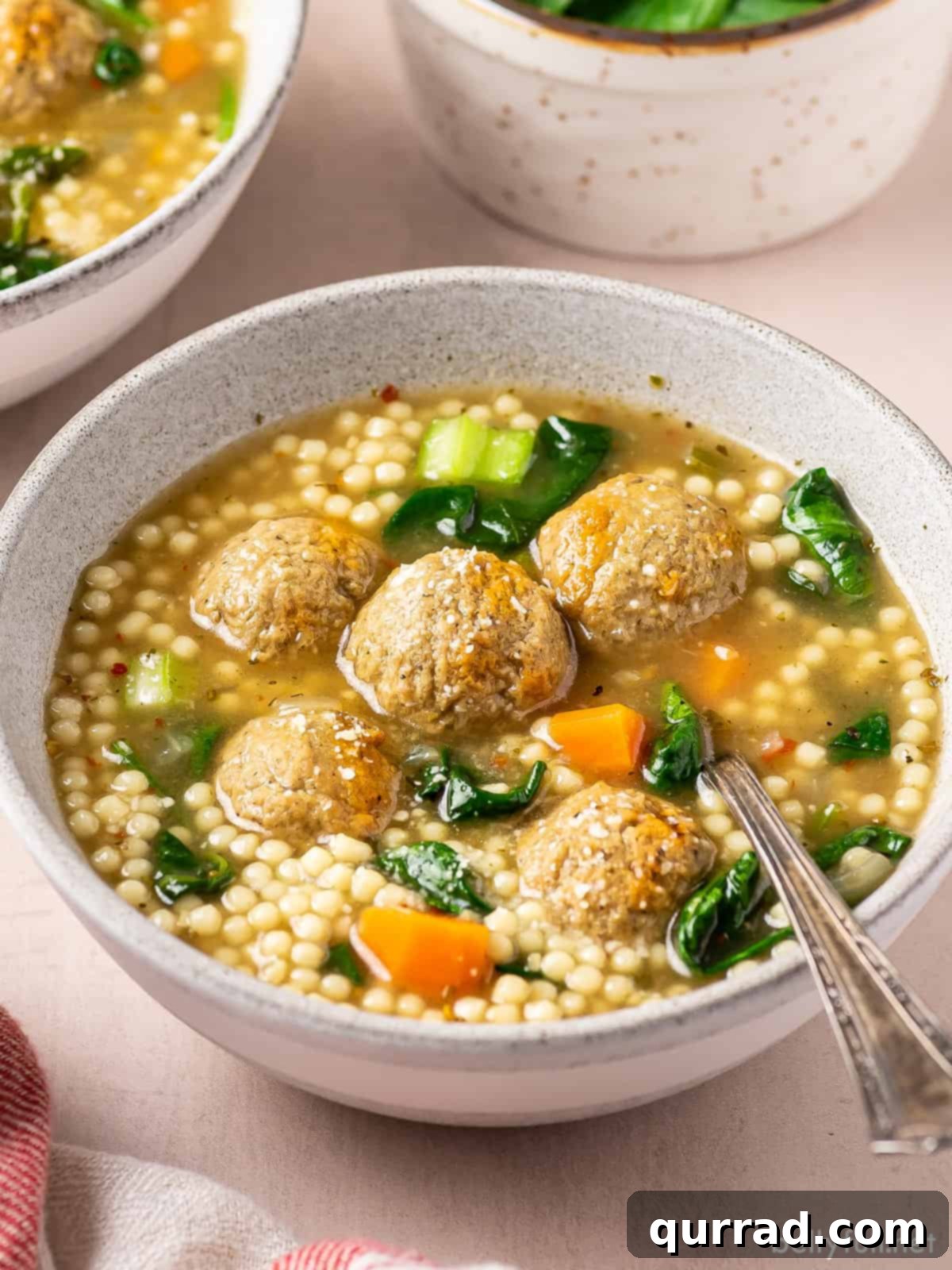 Angled view of a bowl of Italian wedding soup, showcasing the meatballs, pasta, and spinach in a rich broth.