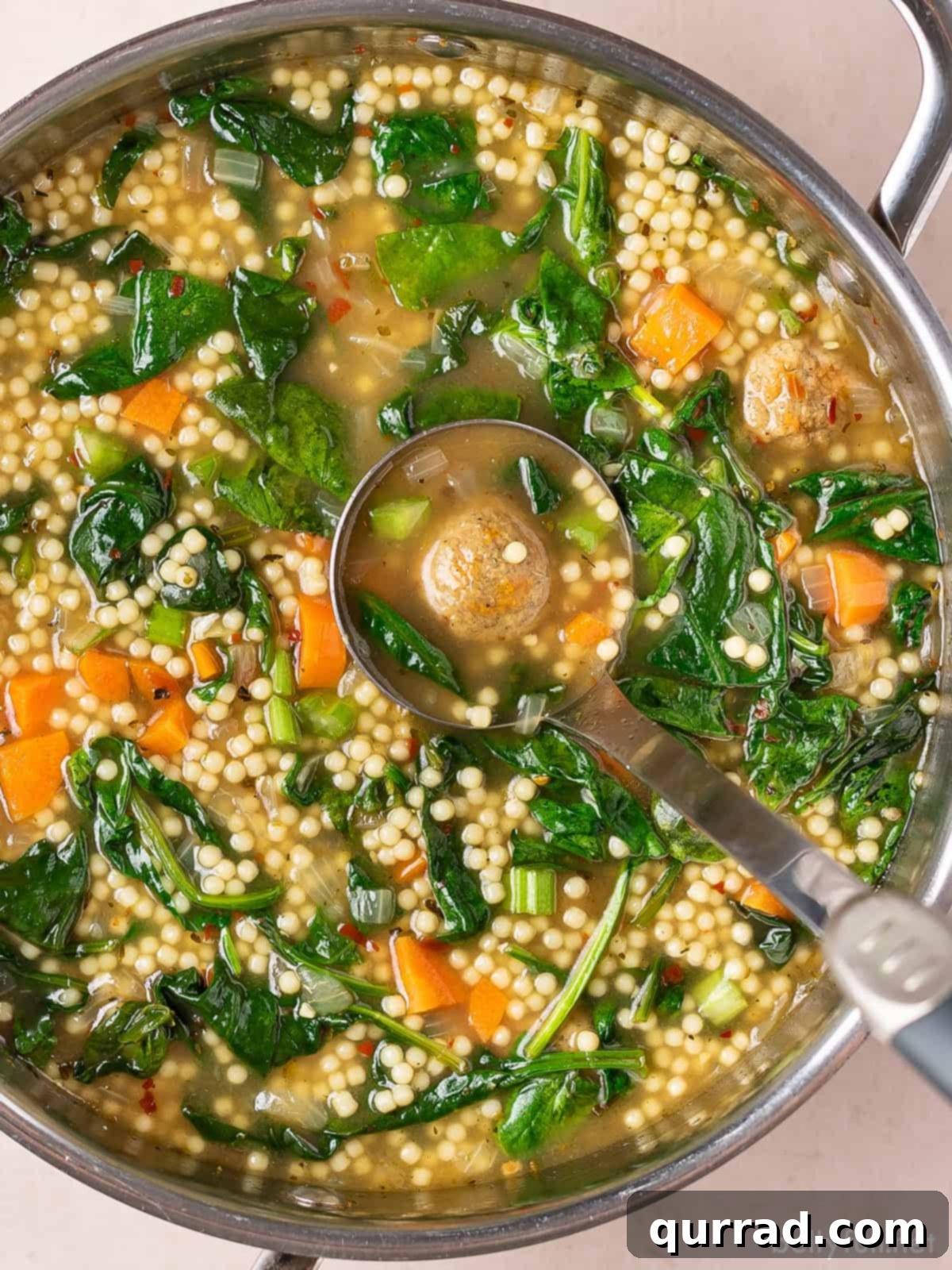 A ladle stirring a pot of Italian wedding soup, showing the vibrant green spinach and small pasta.