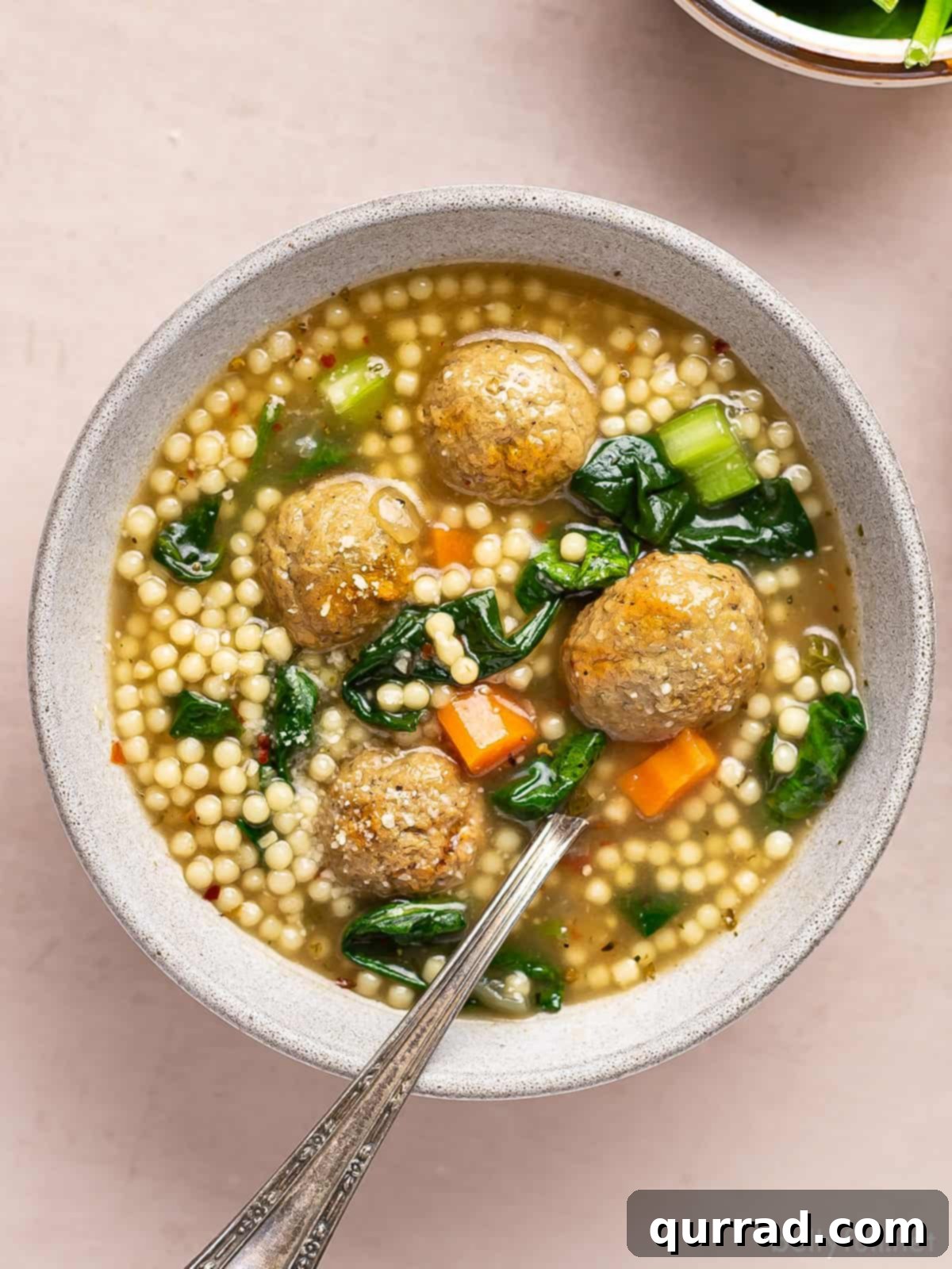 Overhead view of a bowl of Italian wedding soup, garnished with fresh Parmesan.