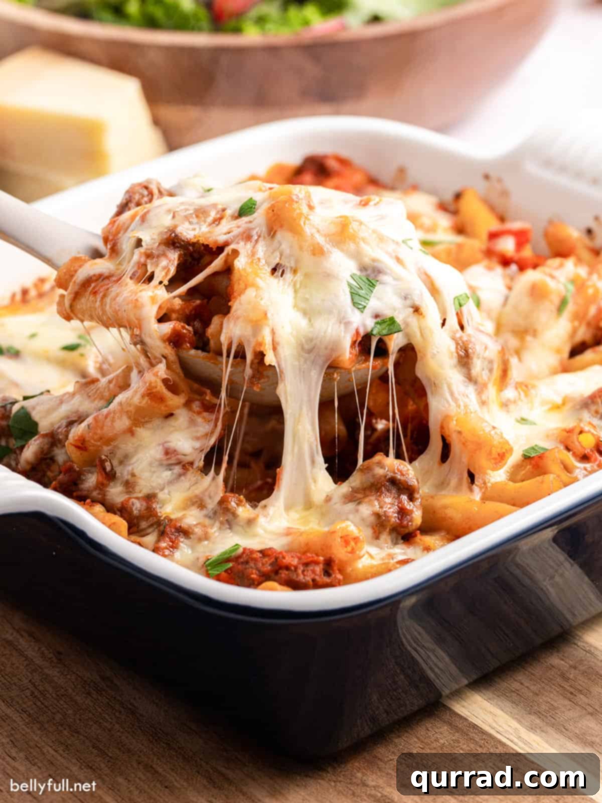 A spoon lifting a serving of baked ziti from the casserole dish