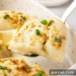 A close-up of a single serving of baked halibut with asparagus on a plate, garnished with fresh scallions and lemon wedges.